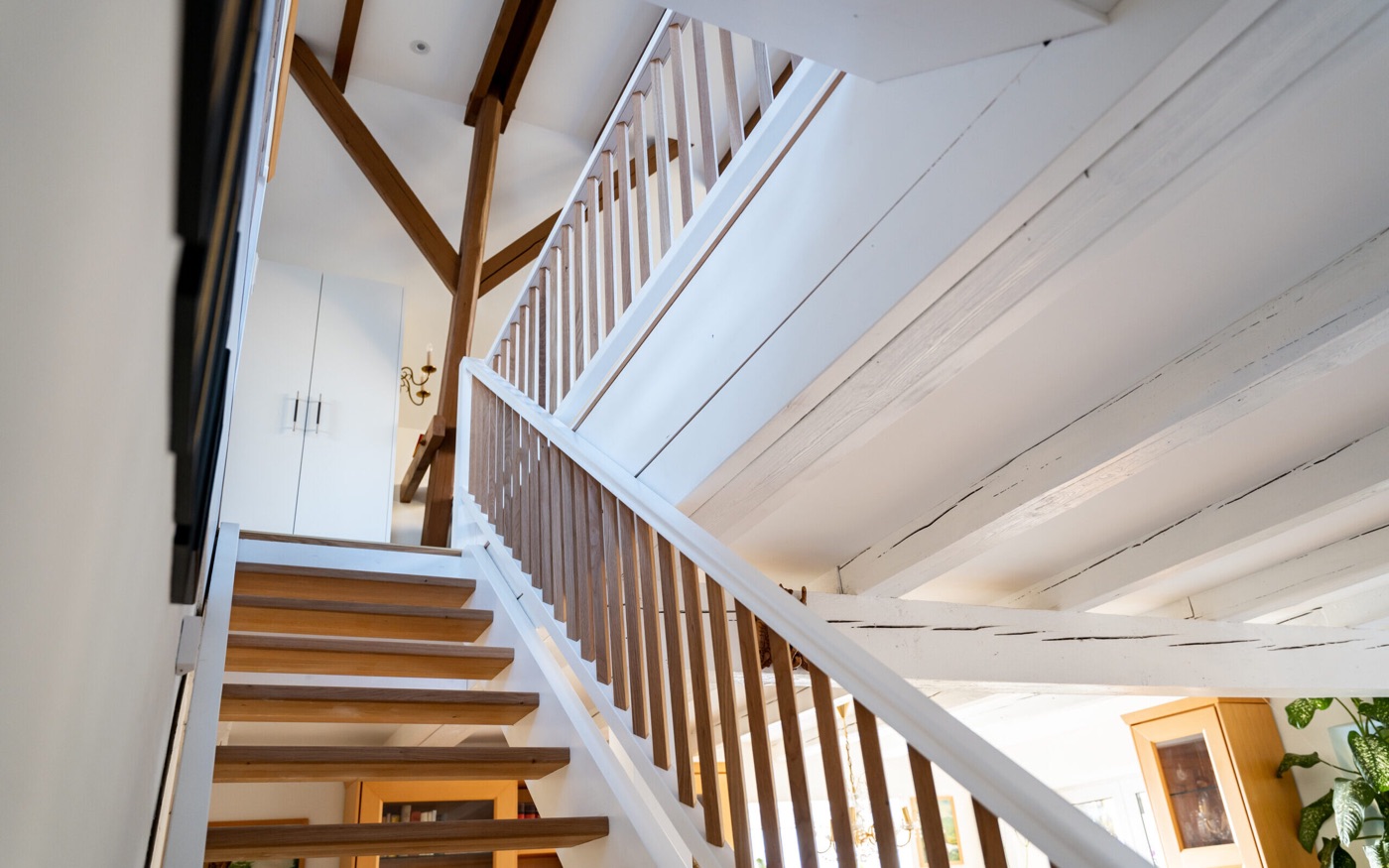 Treppenhaus mit Holzstufen und Holzgeländer unter weiß gestrichenen alten Deckenbalken
