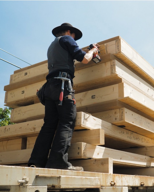 Zimmerer in Kluft arbeitet auf einem Stapel großer Holzbauteile
