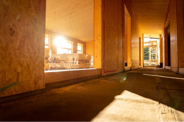 Innenraum des Dorfgemeinschaftshauses im Rohbau mit Holzwänden und Gegenlicht