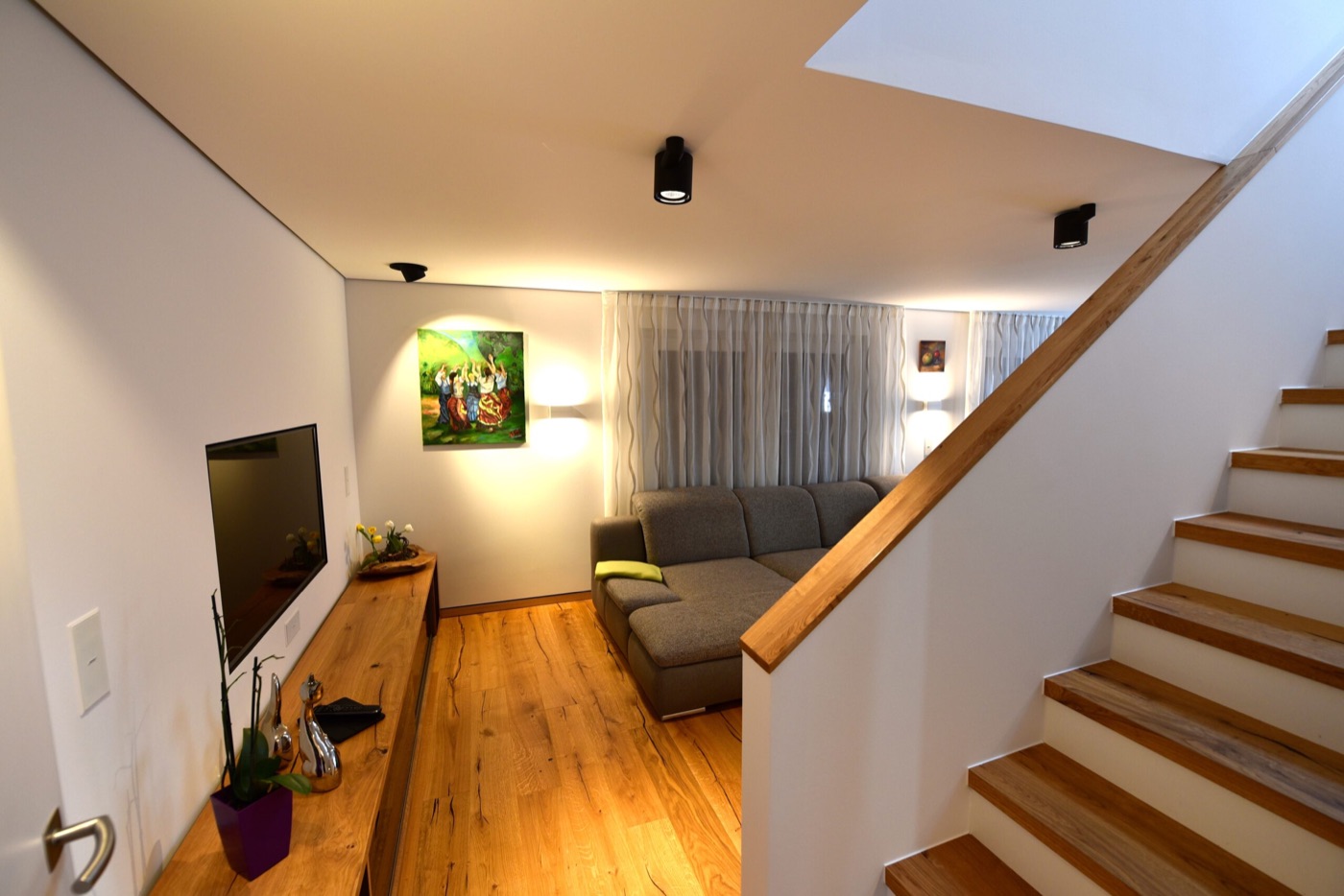 Wohnraum im Musterhaus „Felix“ mit Holztreppe, Holzboden und Sideboard aus Holz