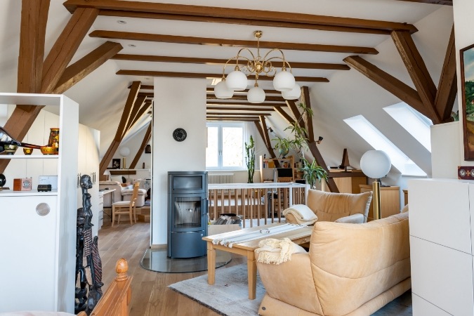 Wohnraum unter dem Dach mit sichtbaren Holzbalken und Kaminofen
