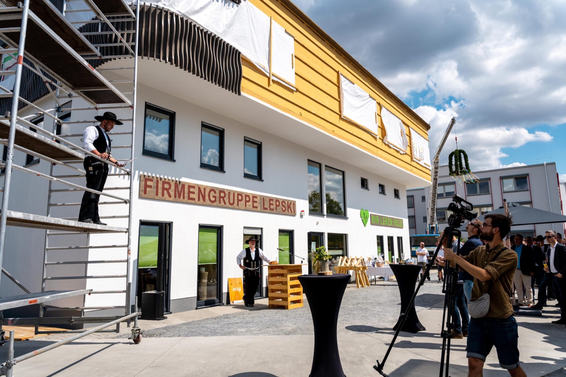 Richtfest am aufgestockten Firmengebäude 2022: Zimmerer in Kluft auf dem Gerüst, darunter Gäste, Rednerpult und Richtkranz