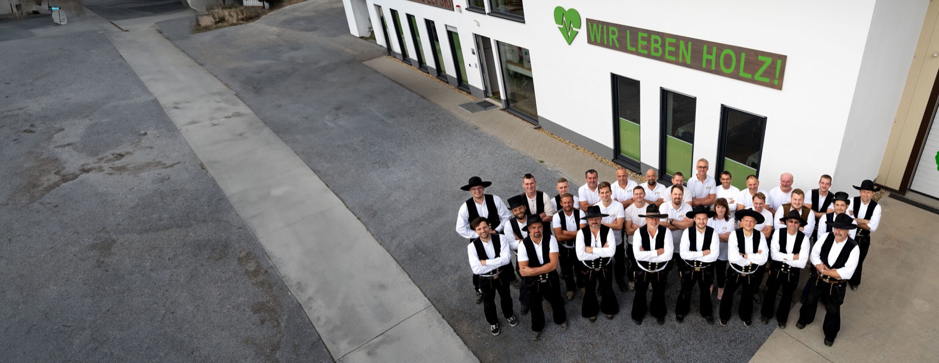 Das Team der Holzbau Lepski GmbH vor dem Firmengebäude in Dresden-Reick, darüber der Schriftzug „Wir leben Holz!“